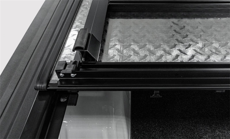LOMAX Hard Tri-Fold tonneau cover: close-up of a lifted panel's silver diamond-plate underside, black frame and hinge