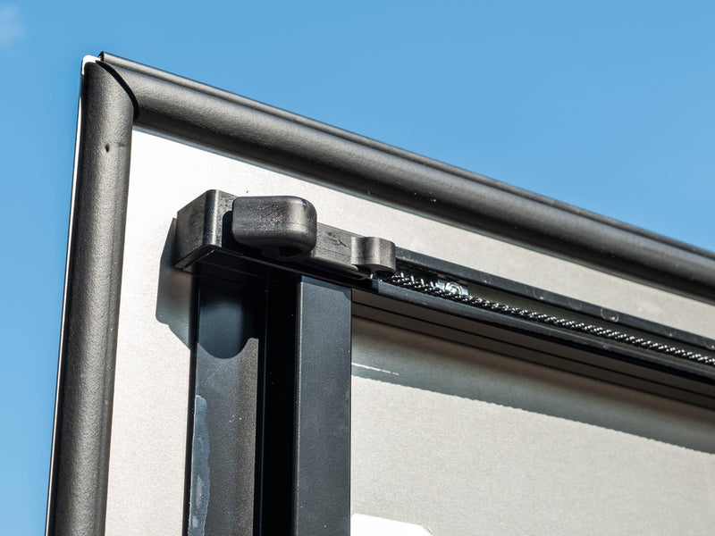 LOMAX Hard Tri-Fold tonneau cover: close-up of a panel corner latch, cable and seal against blue sky