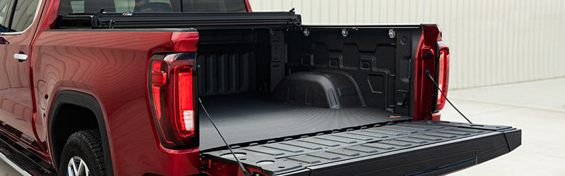 LOMAX Hard Tri-Fold tonneau cover: red pickup with tailgate down, cover folded fully to the cab, rubber bed mat on the floor
