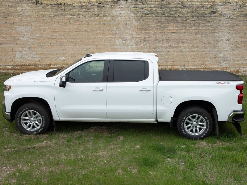 Side profile of a white pickup on grass, low hard tonneau cover closed over the bed