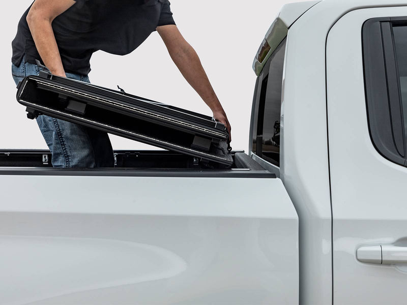Man lifting the folded cover off a white pickup bed
