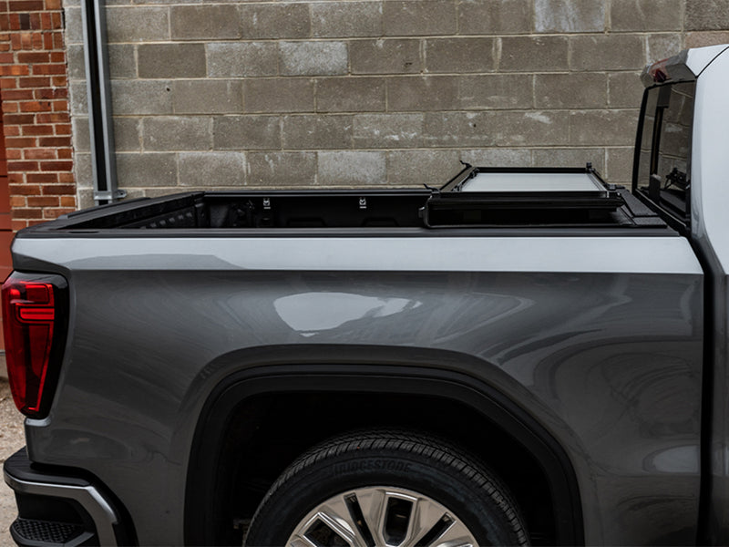 LOMAX STANCE tonneau cover: gray pickup side view at a block wall, cover folded and stacked at the cab