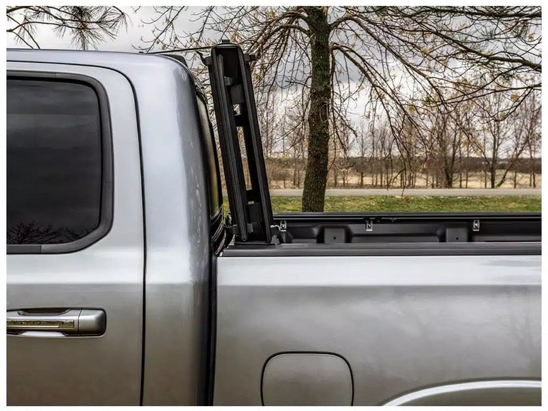 LOMAX STANCE tonneau cover: silver pickup side close-up, STANCE panels stood vertical edge-on against the cab, trees behind