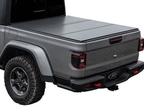 Grey mid-size pickup on white, black hard tri-fold tonneau cover closed, rear three-quarter view