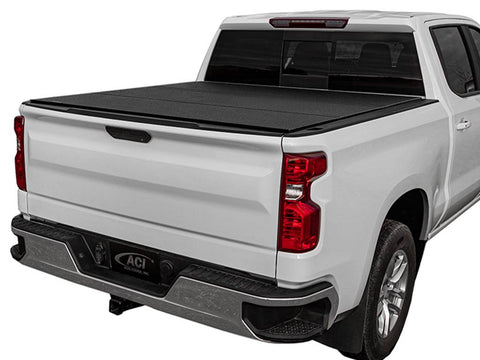 White pickup on white, black hard tri-fold tonneau cover closed flat over the bed, rear three-quarter view