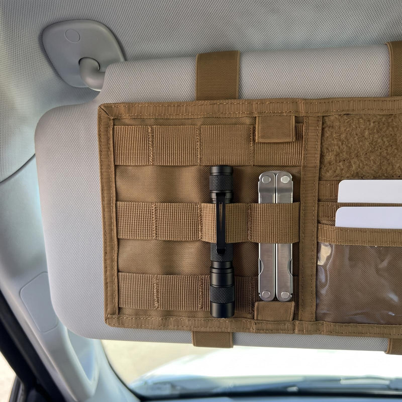 Close-up of the coyote brown organizer's MOLLE webbing on a truck sun visor, with a small black flashlight clipped into one webbing loop, a closed multitool in the next loop and two cards in the card slots