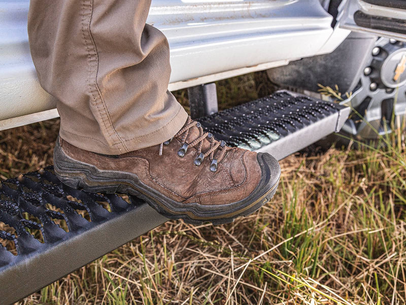 Hiking boot on a N-Fab Growler Fleet grip-plate side step under a white truck in a grass field