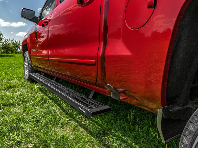 Low view along a red crew-cab pickup on grass showing the full-length N-Fab Growler Fleet grip-plate side step