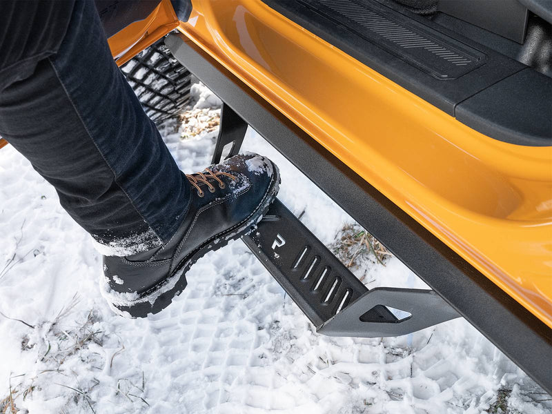 N-Fab Predator Pro nerf steps in textured black, boot on the step at an open door, on a Ford Bronco 4-door