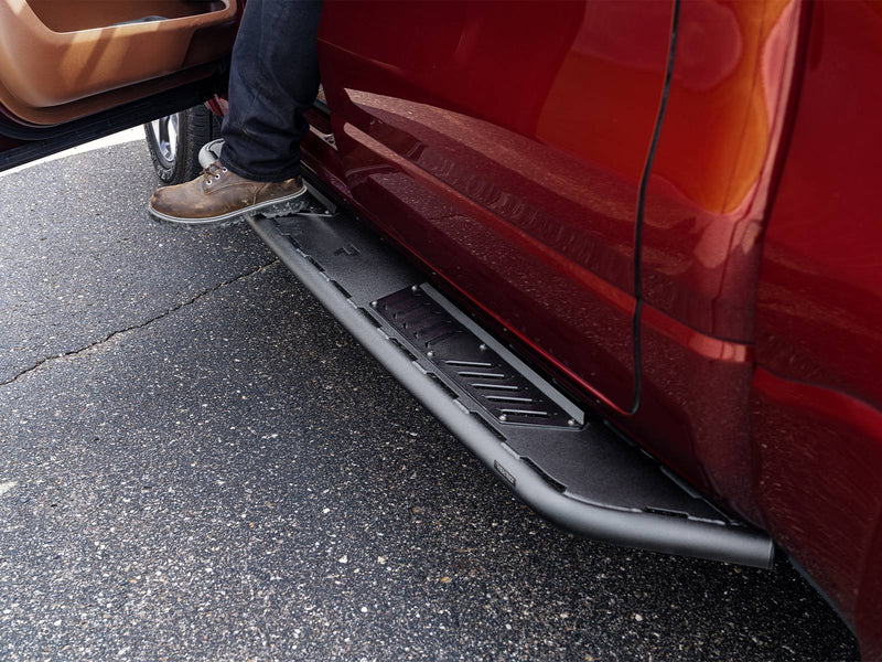 N-Fab Roan running boards in textured black, boot on the step at an open door, on a Ram 1500