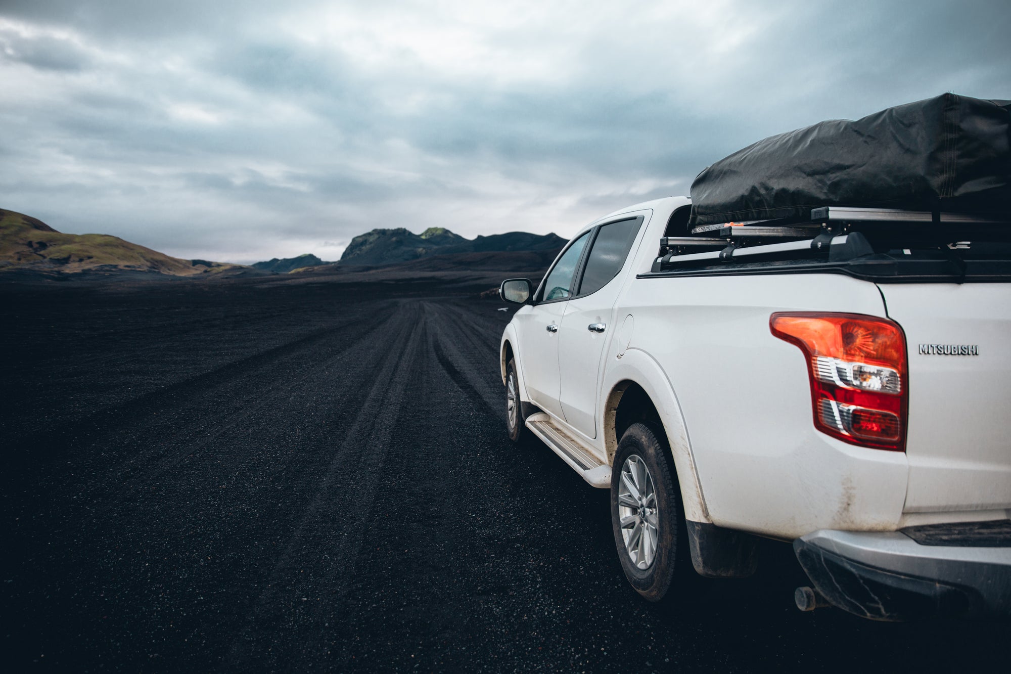 Black pickup truck fitted with off-road bumpers driving across a volcanic sand field at speed