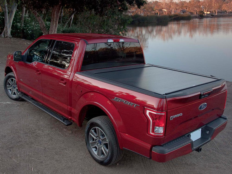 Pace Edwards BedLocker: black retractable cover fully closed on a red pickup parked beside a lake