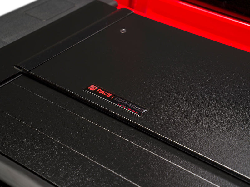Pace Edwards BedLocker: close-up of the black canister lid with a Pace Edwards badge, red bed rail in background