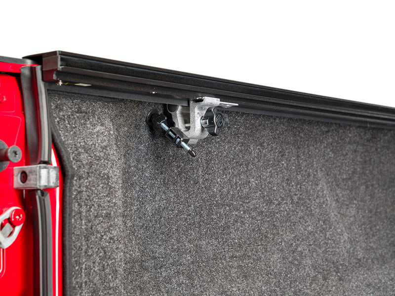 Pace Edwards BedLocker: rail clamp bolted beneath the side rail inside a carpet-lined red truck bed