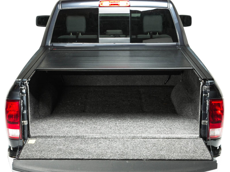Pace Edwards BedLocker: rear view of a black pickup with the retractable cover partly open and tailgate down over a carpeted bed