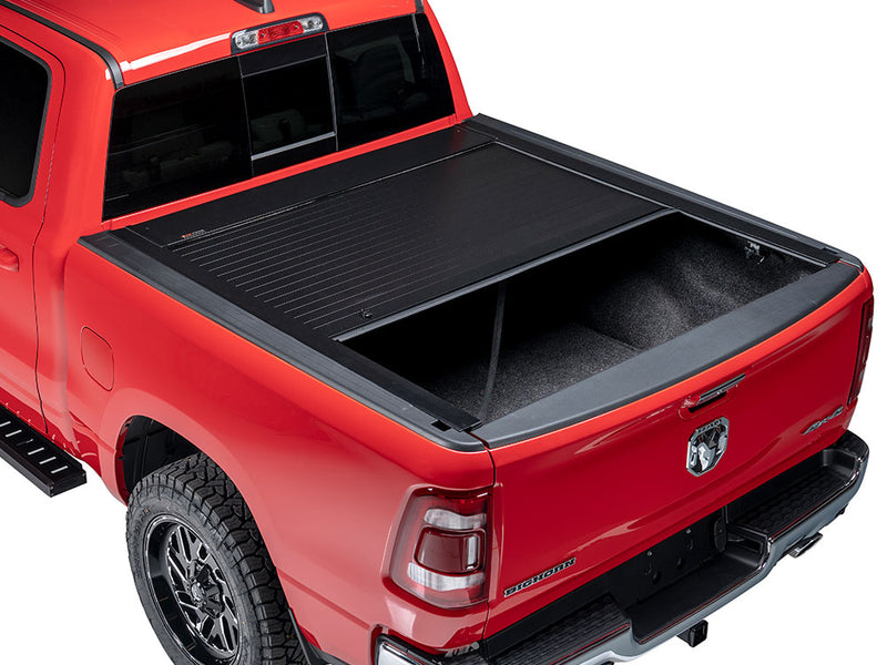 Pace Edwards Full Metal JackRabbit: black retractable cover about half retracted on a red pickup bed, studio rear three-quarter view