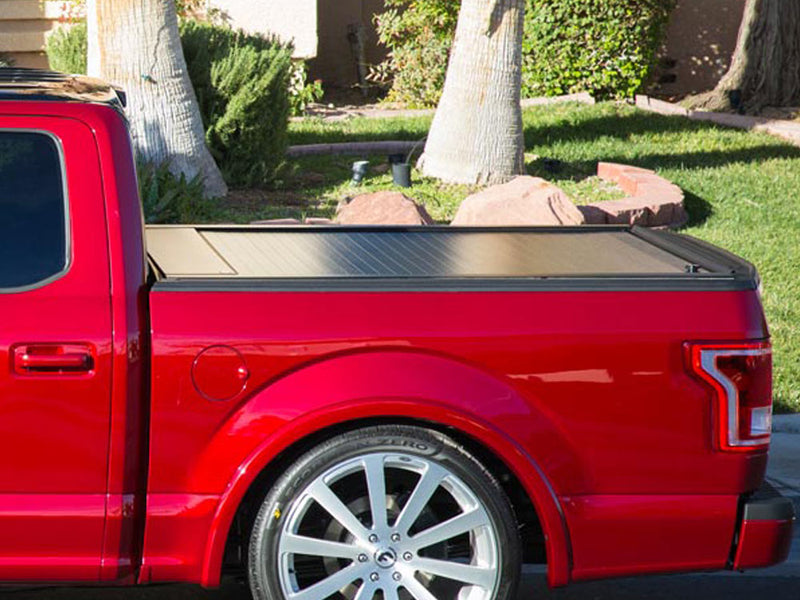 Pace Edwards Full Metal JackRabbit: retractable cover closed on a red pickup bed, side view in a landscaped yard