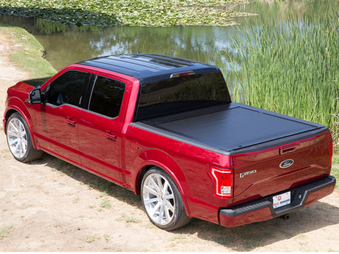 Pace Edwards JackRabbit: black retractable cover fully closed on a red pickup bed by a pond, rear three-quarter view from above
