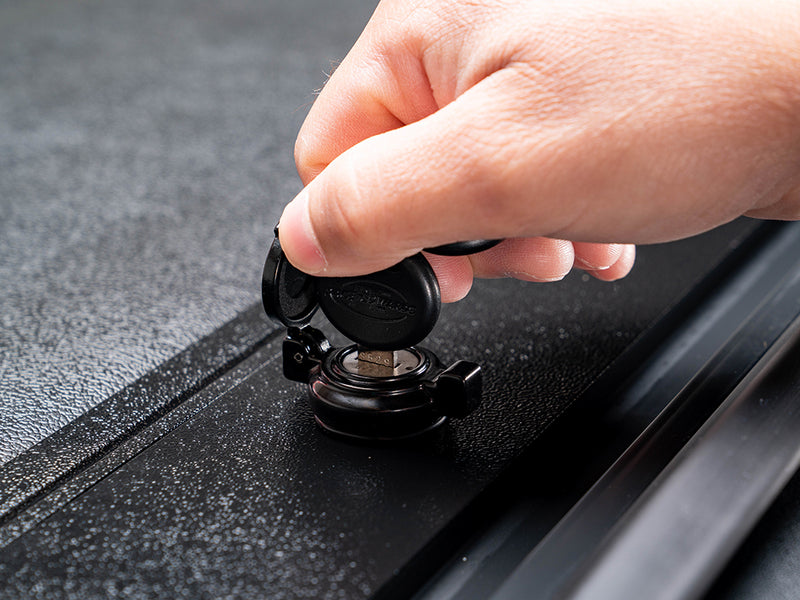 Pace Edwards JackRabbit: hand turns a key in the flip-cap lock on the textured black end slat of the cover