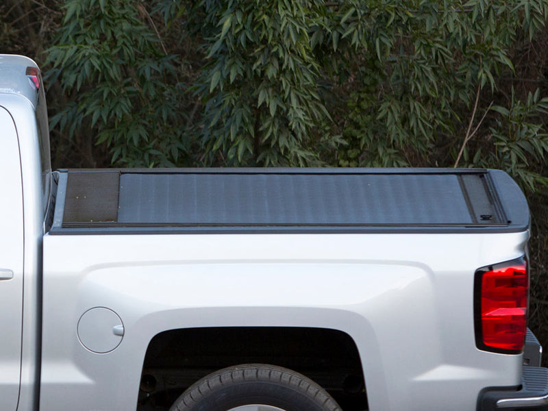 Pace Edwards JackRabbit: side profile of a black retractable cover fully closed on a silver pickup bed, foliage behind