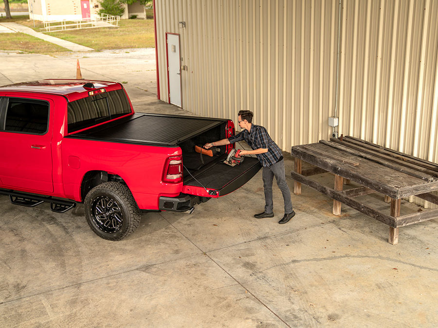 Man sets a circular saw on the lowered tailgate of a red Ram 1500 with a closed black retractable cover