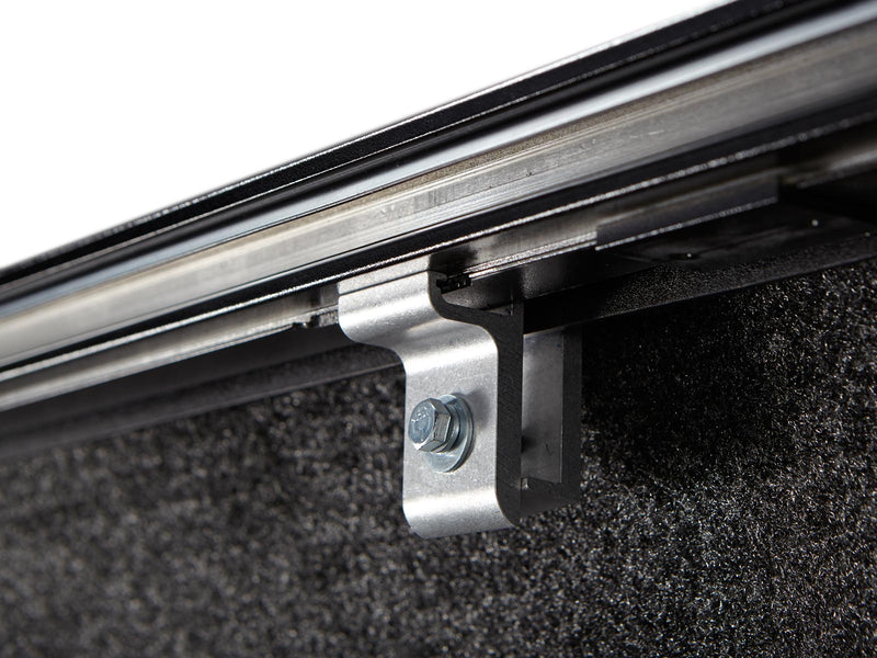 Pace Edwards SwitchBlade: close-up of a metal clamp bolting the side rail to the bed wall under a retractable cover, carpeted bed
