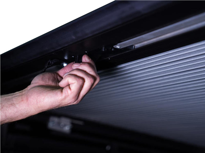 Pace Edwards SwitchBlade: hand reaching up to the latch under a closed retractable cover at the tailgate end of the rail
