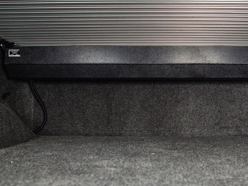 Pace Edwards SwitchBlade: inside-bed view of the retractable cover canister at the bulkhead with drain tube, slats closed overhead, carpeted liner