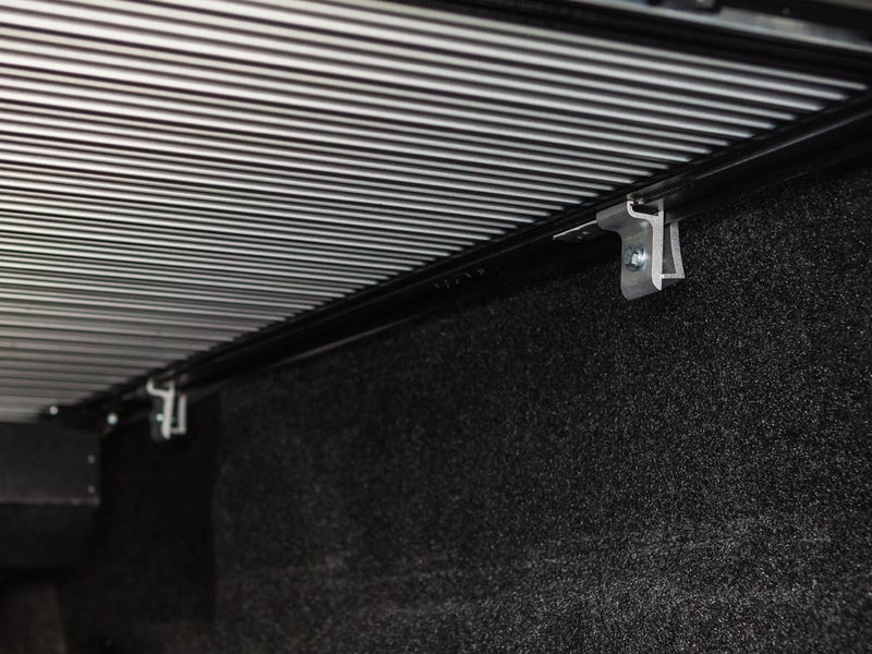 Pace Edwards SwitchBlade: underside view of closed aluminum cover slats and side rail clamps inside a carpeted truck bed