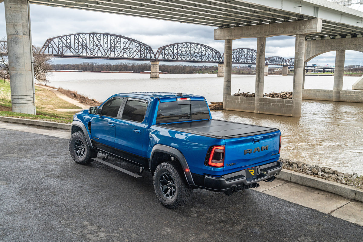 UnderCover Ultra Flex hard folding tonneau cover on a blue Ram 1500 TRX by a river