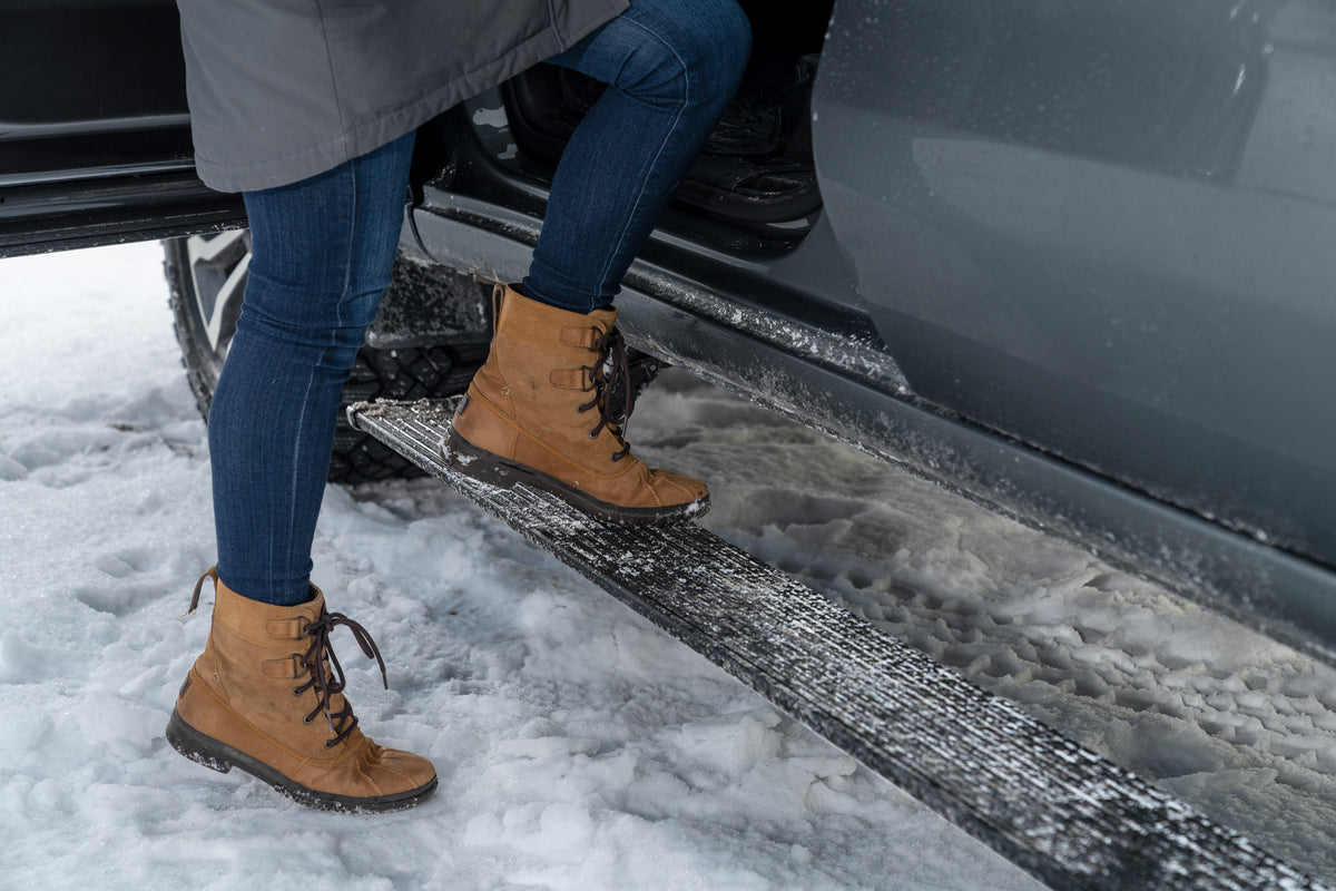 Winter boot on an AMP PowerStep electric running board of a gray GMC Sierra in snow
