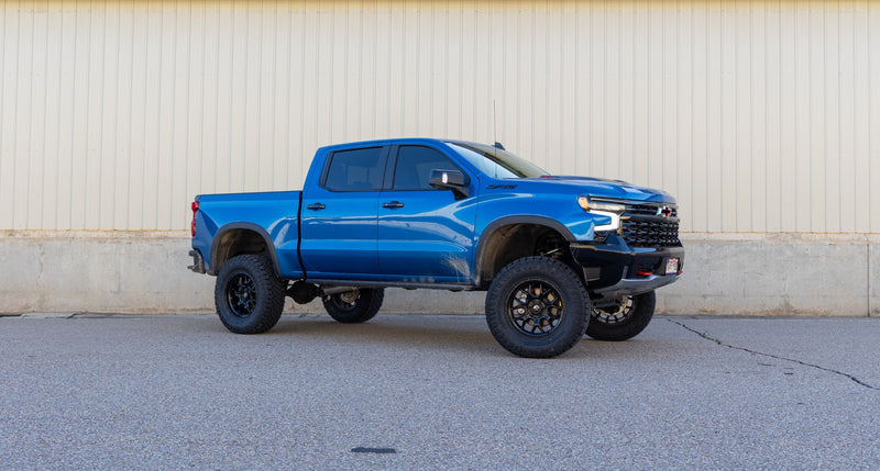 ReadyLIFT Big Lift Kit installed on a Chevrolet Silverado 1500 ZR2: blue Chevrolet Silverado ZR2 crew cab lifted on black wheels, side profile against a concrete wall