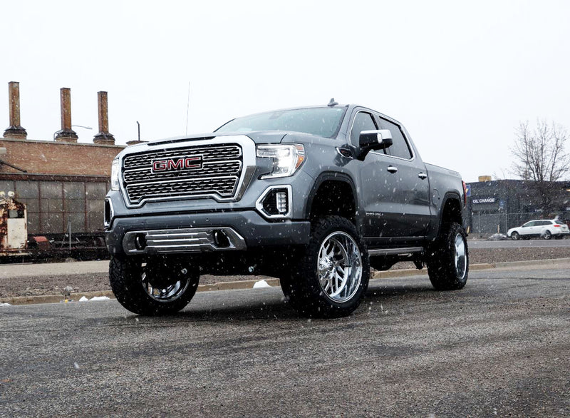 ReadyLIFT Big Lift Kit installed on a GMC Sierra 1500 Denali: gray GMC Sierra 1500 Denali crew cab lifted on chrome wheels in light snow beside an industrial rail yard