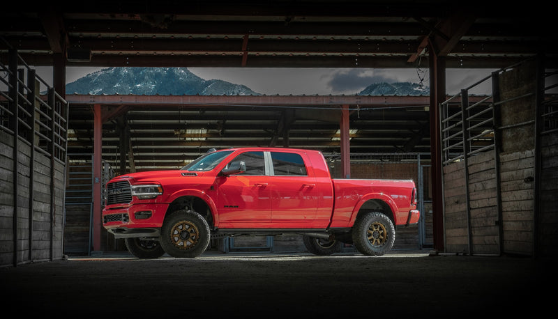 ReadyLIFT Coil Spring Leveling Kit installed on a Ram 2500 Mega Cab: red Ram 2500 Mega Cab leveled on bronze wheels inside a dark timber barn opening to mountains