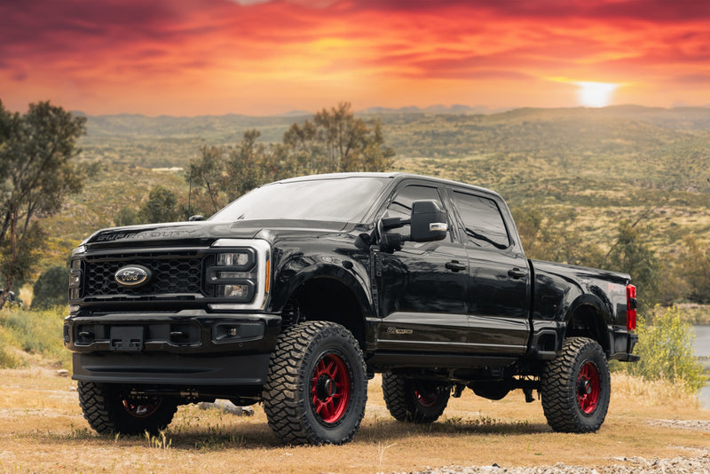 ReadyLIFT Coil Spring Lift Kit installed on a Ford F-250 Super Duty: black Ford Super Duty crew cab lifted on red wheels under an orange sunset sky