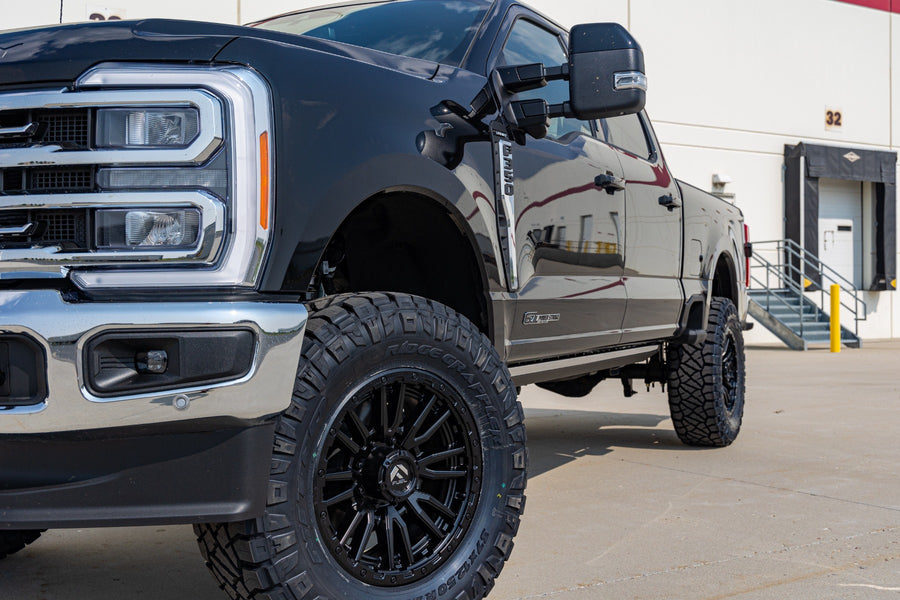 ReadyLIFT Coil Spring Lift Kit on a Ford F-250 Super Duty: close front quarter of a black Ford Super Duty lifted on black wheels and mud tires