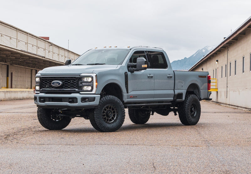 ReadyLIFT Coil Spring Lift Kit installed on a Ford F-250 Super Duty: gray Ford Super Duty Tremor crew cab lifted on black wheels between warehouse buildings