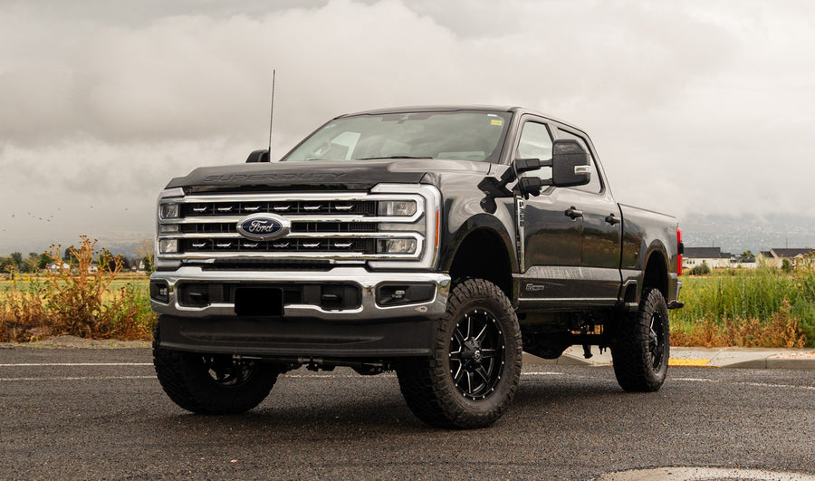 ReadyLIFT Coil Spring Suspension System installed on a Ford F-250 Super Duty: black Ford Super Duty crew cab lifted on black wheels on a wet lot under cloudy sky