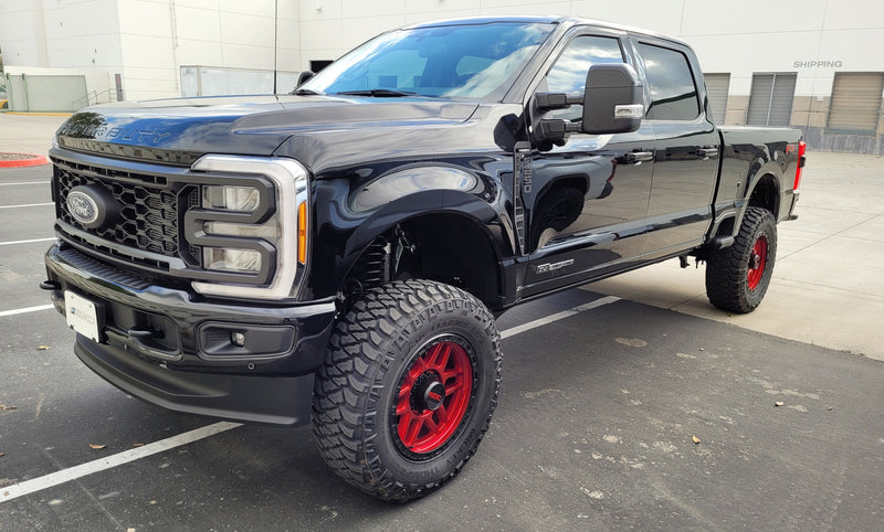 ReadyLIFT Coil Spring Suspension System installed on a Ford F-250 Super Duty: black Ford Super Duty crew cab lifted on red wheels in a parking lot