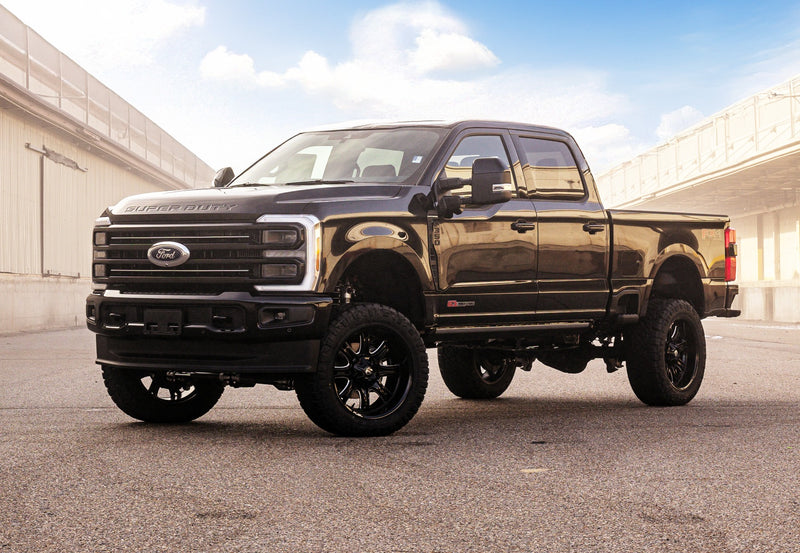 ReadyLIFT Coil Spring Suspension System installed on a Ford F-250 Super Duty: dark Ford Super Duty crew cab lifted on black wheels between warehouse buildings in warm light