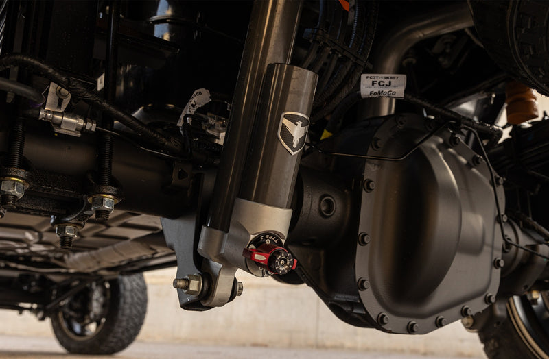 ReadyLIFT Coil Spring Suspension System on a vehicle: Falcon reservoir shock with red adjuster installed next to a heavy-duty rear axle under a truck