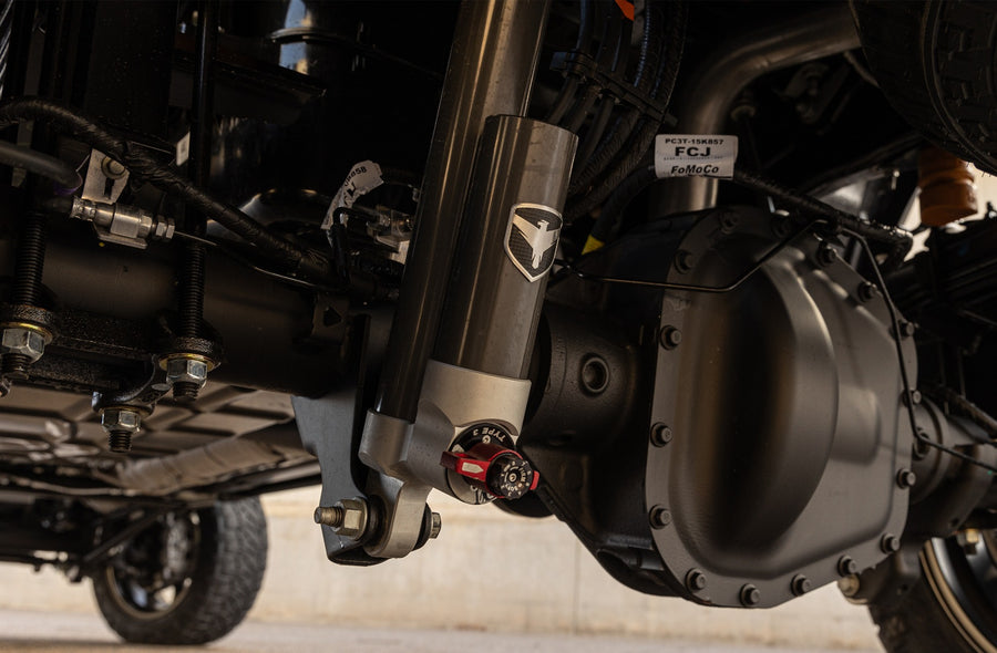 ReadyLIFT Coil Spring Suspension System on a vehicle: Falcon reservoir shock with red adjuster installed next to a heavy-duty rear axle under a truck