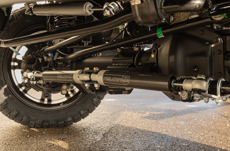 ReadyLIFT Coil Spring Suspension System on a vehicle: low view under a Super Duty front axle showing installed stabilizer and Falcon shocks on wet pavement