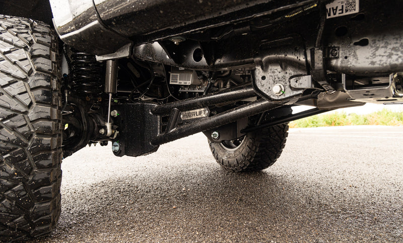 ReadyLIFT Coil Spring Suspension System on a vehicle: low view under a Super Duty showing the installed ReadyLIFT radius arm behind a mud tire