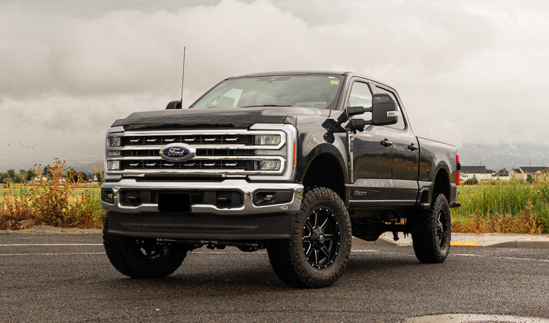 ReadyLIFT Coilover Suspension System installed on a Ford F-250 Super Duty: black Ford Super Duty crew cab lifted on black wheels on a wet lot beside a field