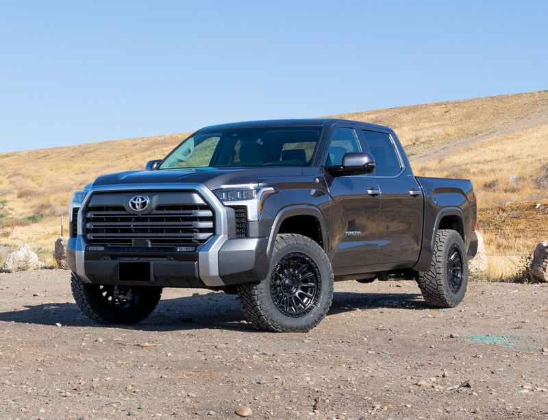 ReadyLIFT Leveling Kit installed on a Toyota Tundra: gray Toyota Tundra crew cab leveled on black wheels on dry dirt beside a hill, plate blanked