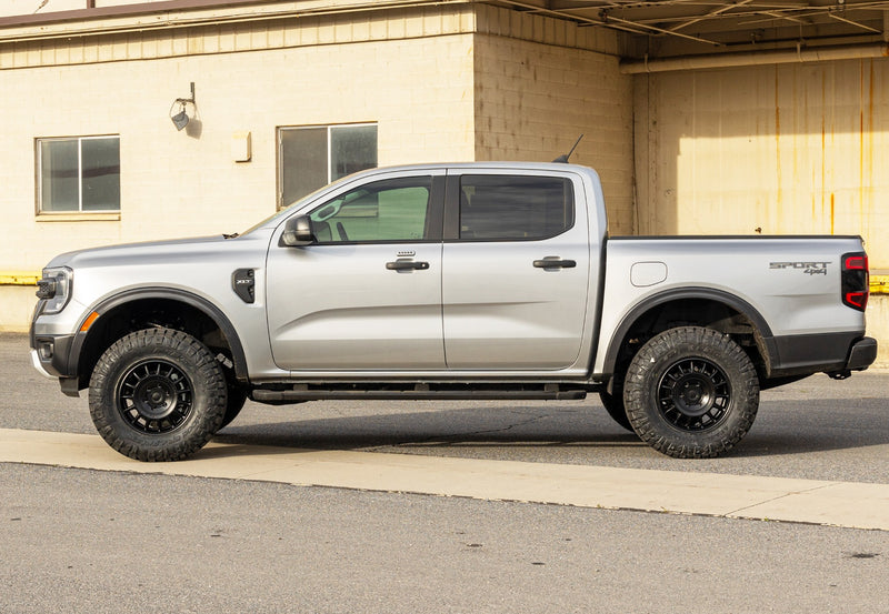 ReadyLIFT Leveling Kit installed on a Ford Ranger: silver Ford Ranger Sport crew cab leveled on black wheels, side profile beside a warehouse
