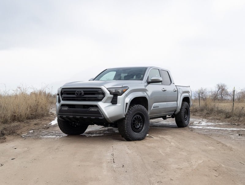 ReadyLIFT Leveling Kit installed on a Toyota Tacoma: silver fourth-generation Toyota Tacoma crew cab leveled on black wheels on a muddy dirt track