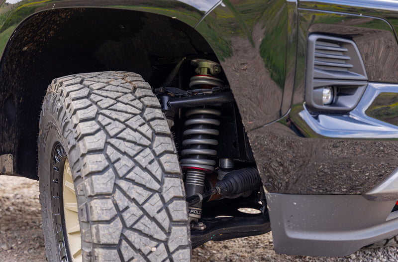 ReadyLIFT Lift Kit on a vehicle: close-up of an installed Falcon coilover behind an all-terrain tire in a black truck wheel well