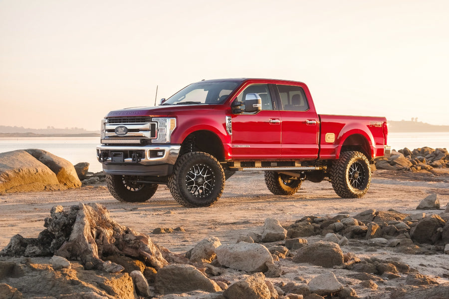 ReadyLIFT Lift Kit installed on a Ford F-250 Super Duty: red Ford Super Duty crew cab lifted on black wheels on a rocky shoreline